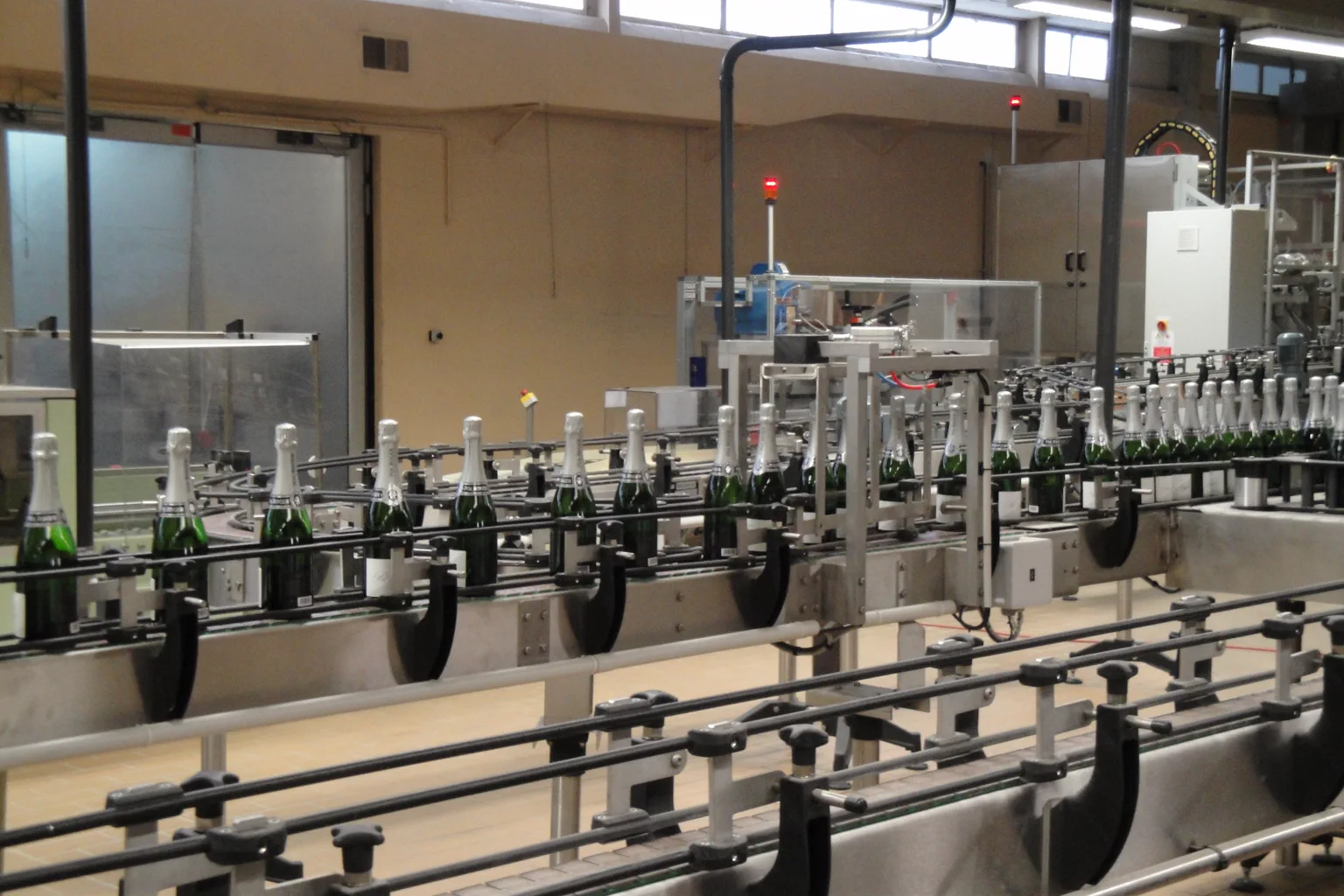 Labeled sparkling-wine bottles moving through an automatic industrial labeling line with stainless steel conveyors
