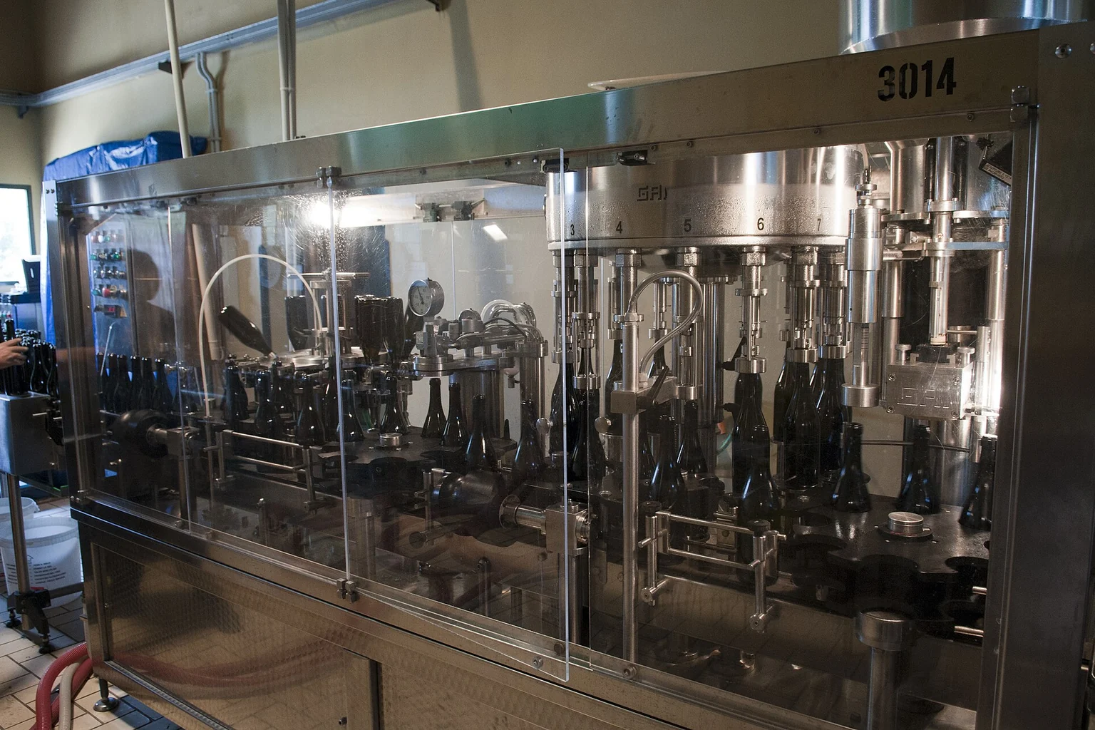 Industrial rotary bottle filling machine operating behind a safety enclosure