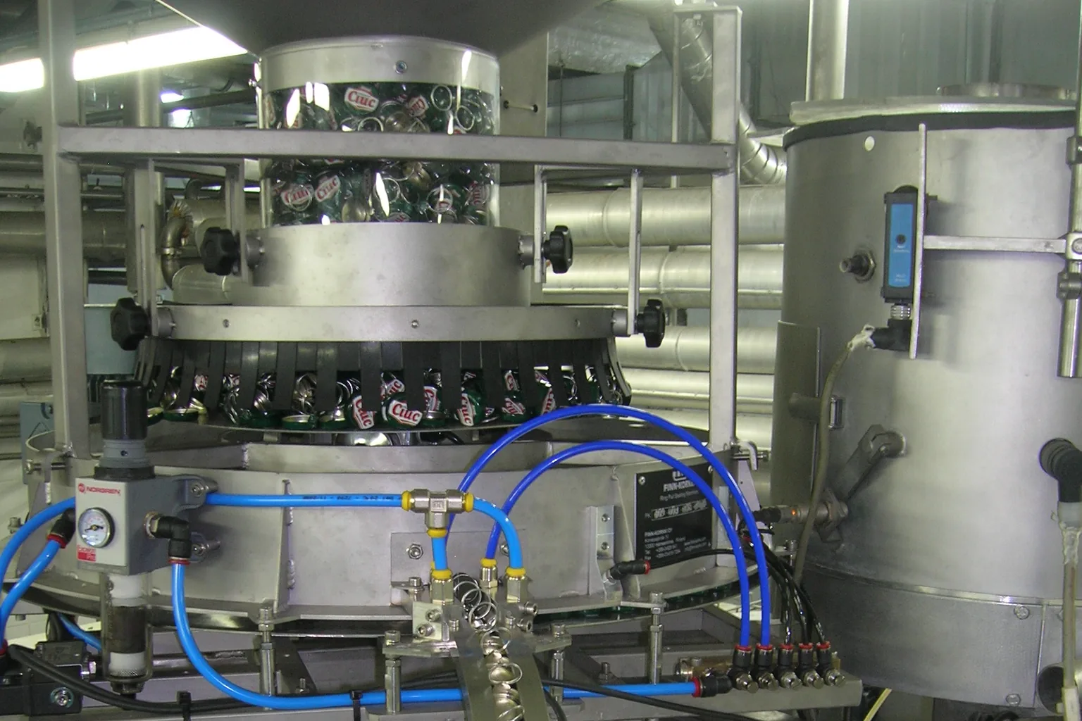 Industrial cap sorting hopper and metal chute feeding closures toward a bottle capping turret