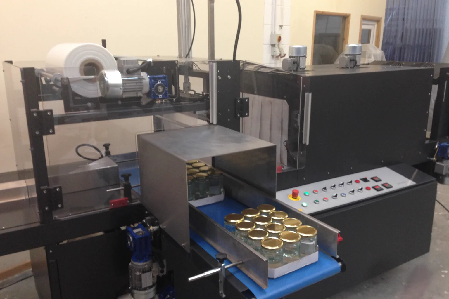 Industrial shrink wrapping machine grouping capped glass jars on a conveyor before the heat tunnel