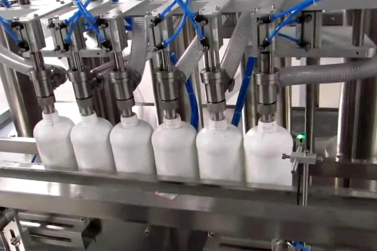 Stainless steel multi-nozzle machine filling opaque plastic detergent bottles on an industrial conveyor