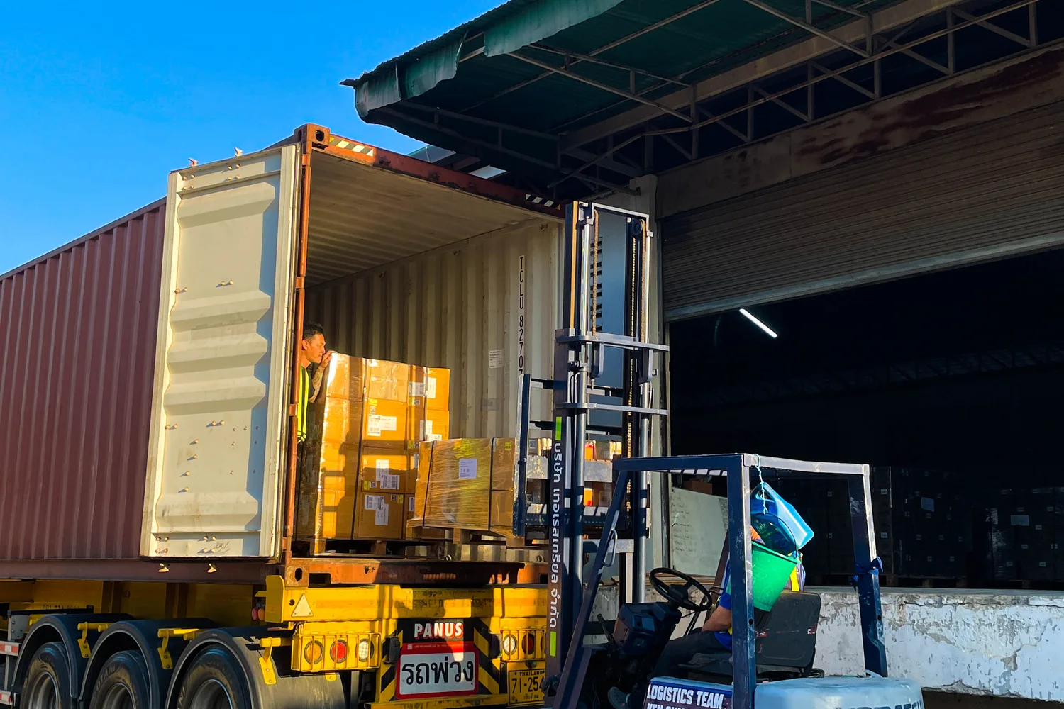 Warehouse workers using a forklift to load palletized cargo into an open shipping container